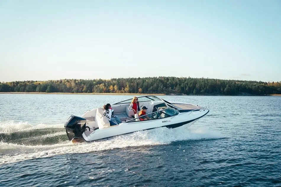 A speedboat navigates a lake with three passengers onboard, surrounded by trees and a clear blue sky.